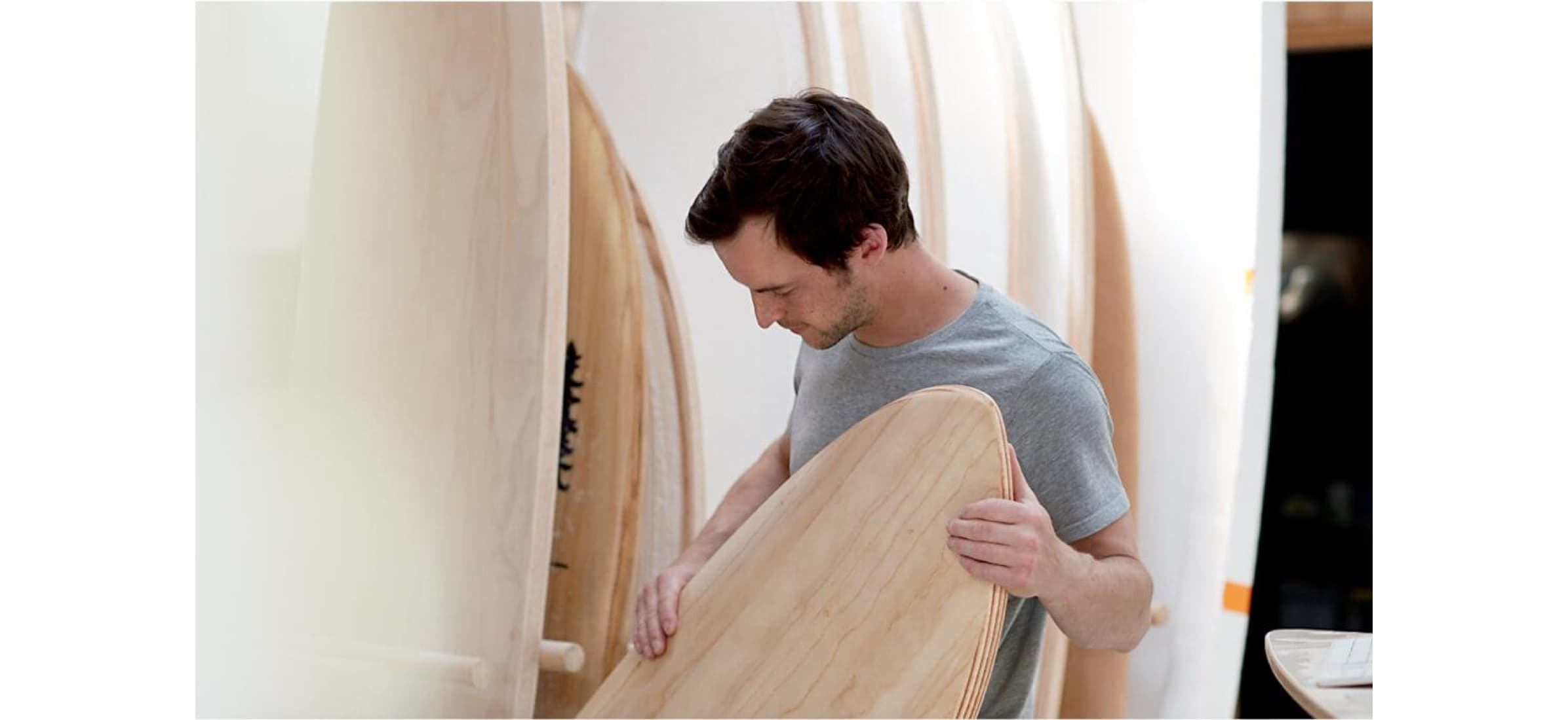Jack putting one of their wooden surfboards in a rack of other surfboards of various sizes.